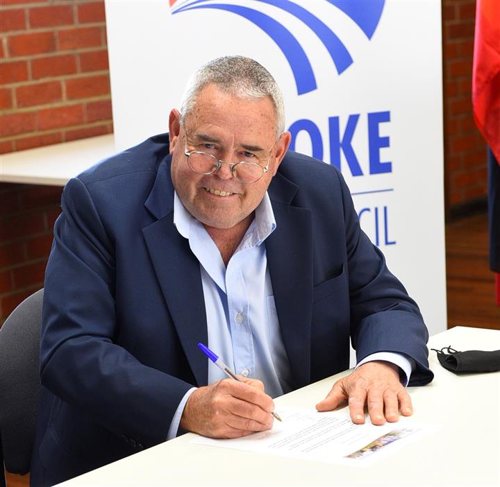 A portrait of Daryl Warren, signing council documents in front of a Buloke banner